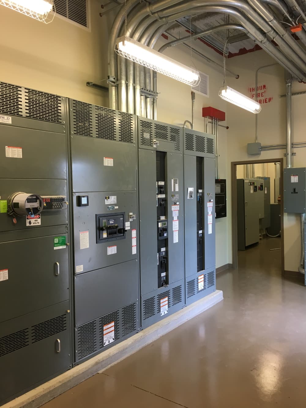 Commercial electrical switchgear lineup with overhead conduit runs and 480-volt service in a mechanical room, installed by H&M Electric